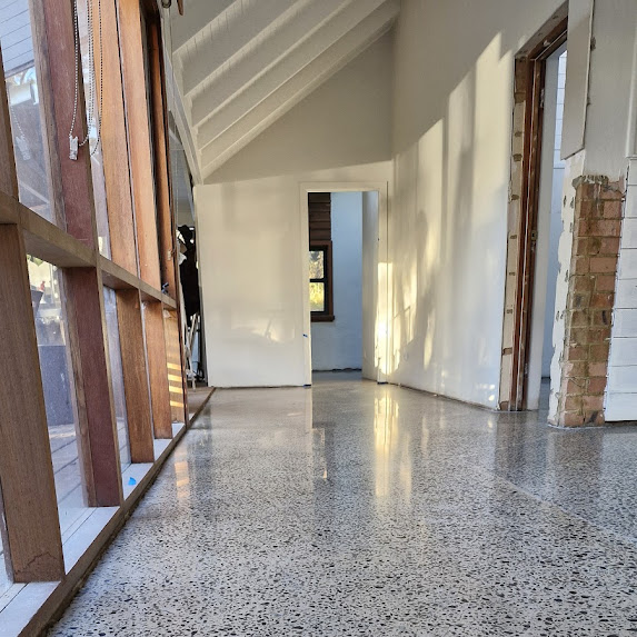 Polished concrete floor in a corridor with white walls, large windows on the left, and sunlight streaming in. Doorways lead to other rooms in the background.