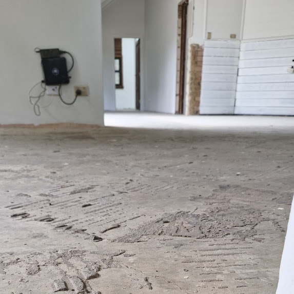 Room with unfinished, textured concrete floor; white walls; exposed wiring on the left wall; and partially open doorway in the background.