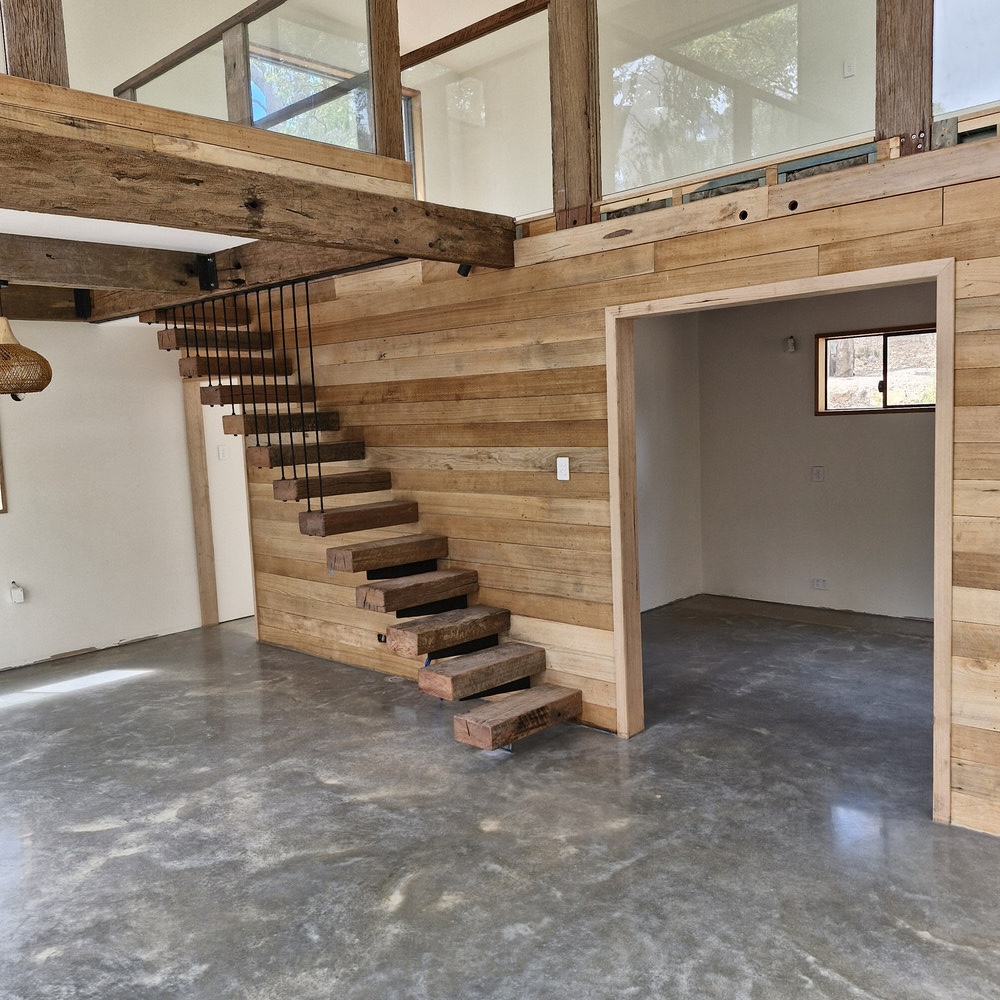 Modern rustic interior with timber floating stairs and concrete floor.