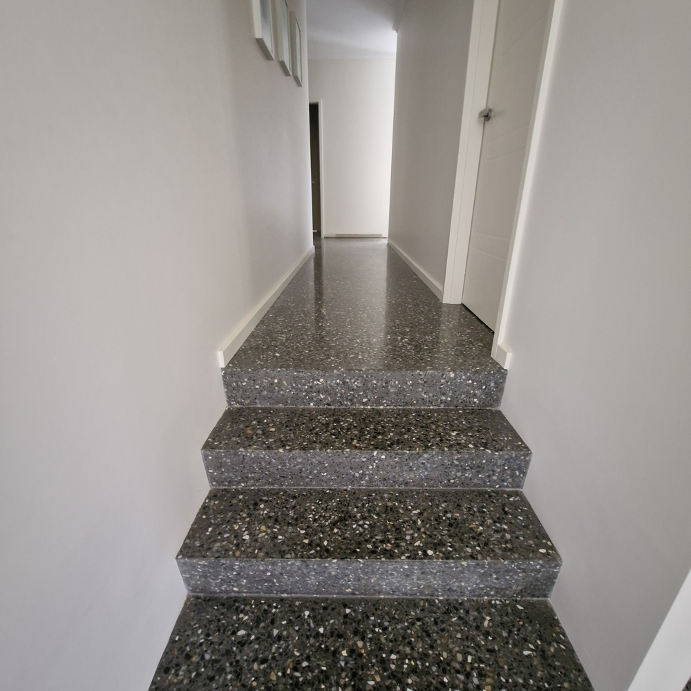 Modern polished dark grey terrazzo stairs in a bright hallway.