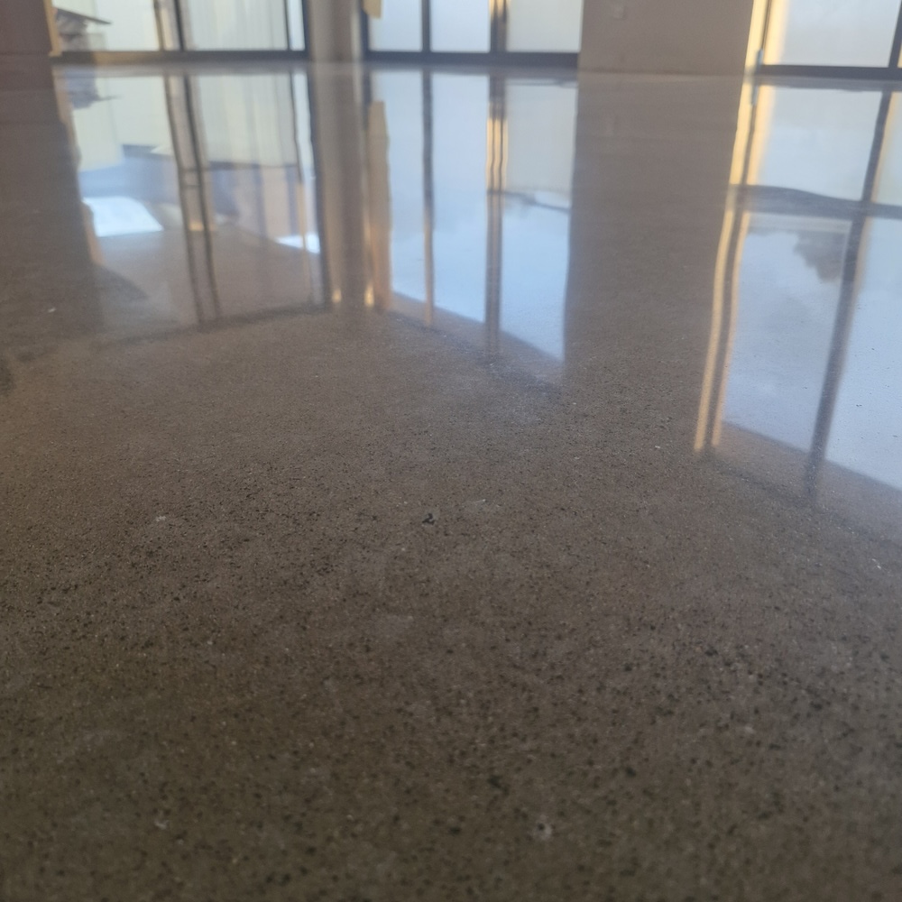 Polished concrete floor reflecting light from large glass windows.